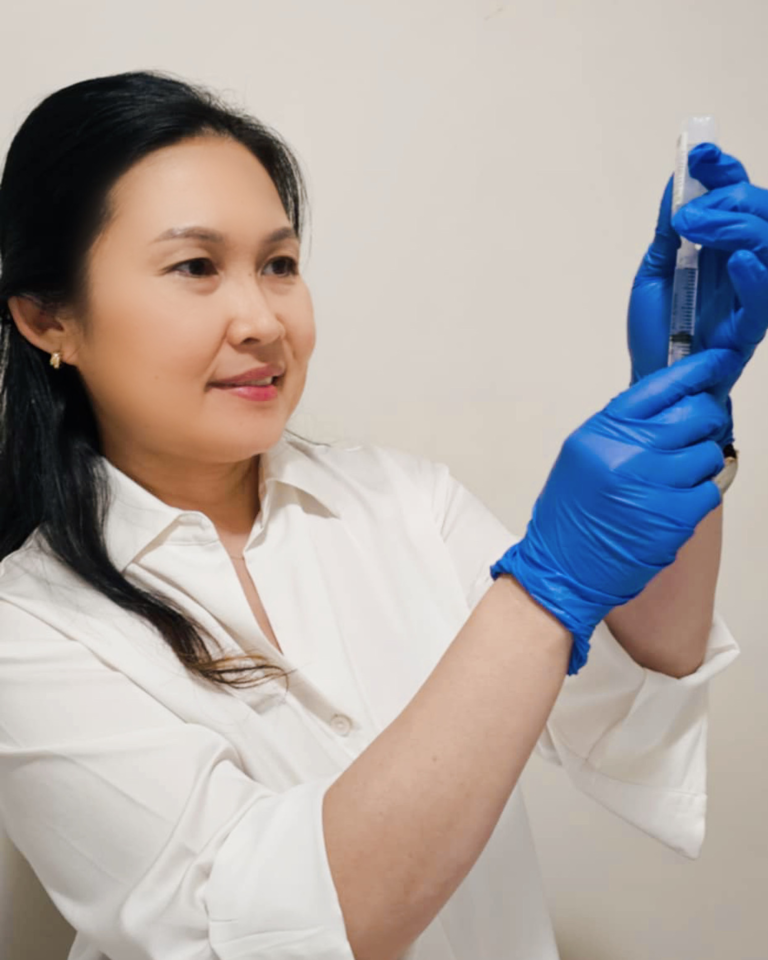 A professional portrait of Precilla Sharp, RN, the founder of The Contour Hub Cosmetic Clinic in Sydney, wearing blue gloves while precisely preparing a treatment syringe.