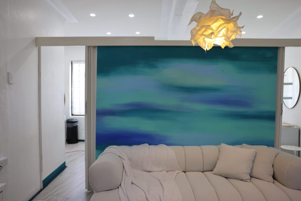 The Contour Hub Advanced Skin & Aesthetic Clinic waiting area in Auburn featuring a modern cream channel-tufted sofa, textured white throw blanket, and a striking teal blue abstract feature wall under a warm pendant light.