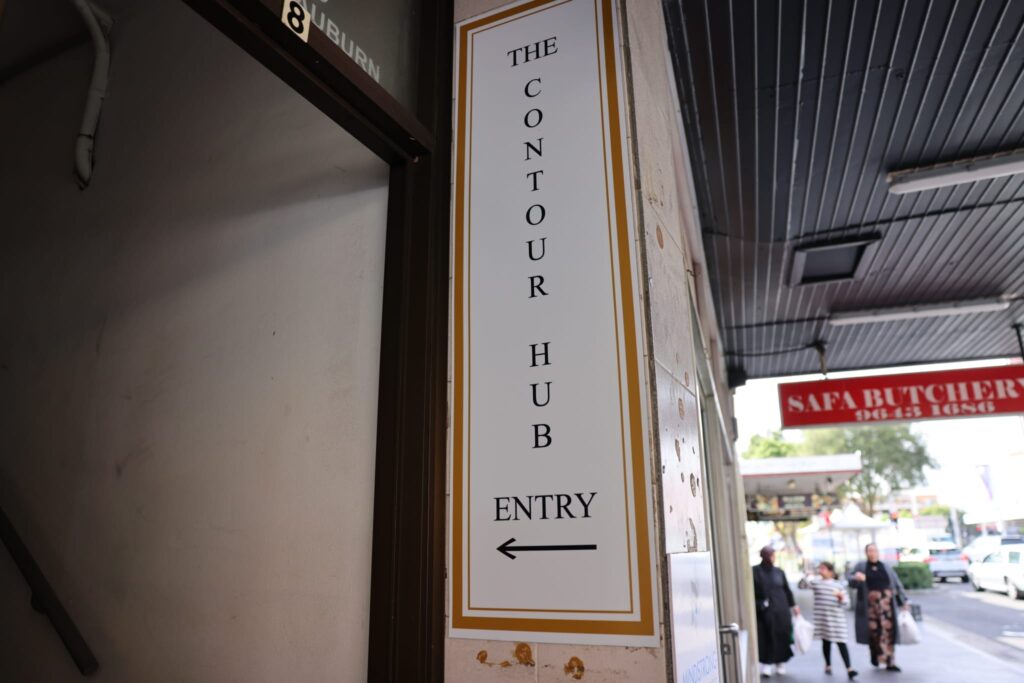 The Contour Hub vertical entry wall sign with an arrow pointing toward the clinic staircase entrance on Auburn Road.
